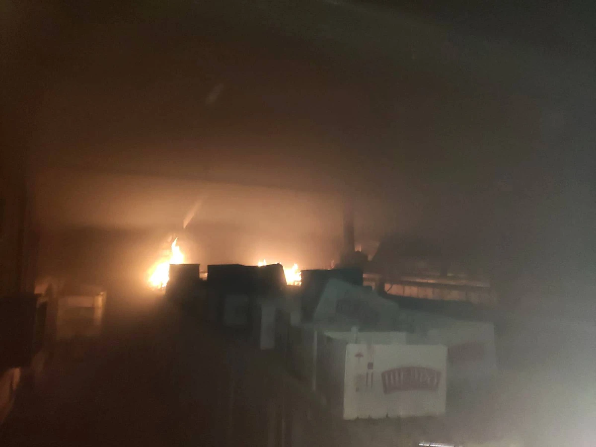 A blaze glows through thick smoke above a row of buildings at night