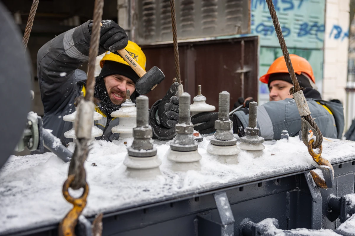 Ремонтная бригада расчищает новый трансформатор от снега и льда перед тем, как установить его на подстанцию