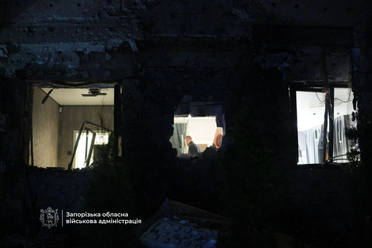 Shattered window openings in a heavily damaged building, revealing people inside amid the darkened remains of the structure.