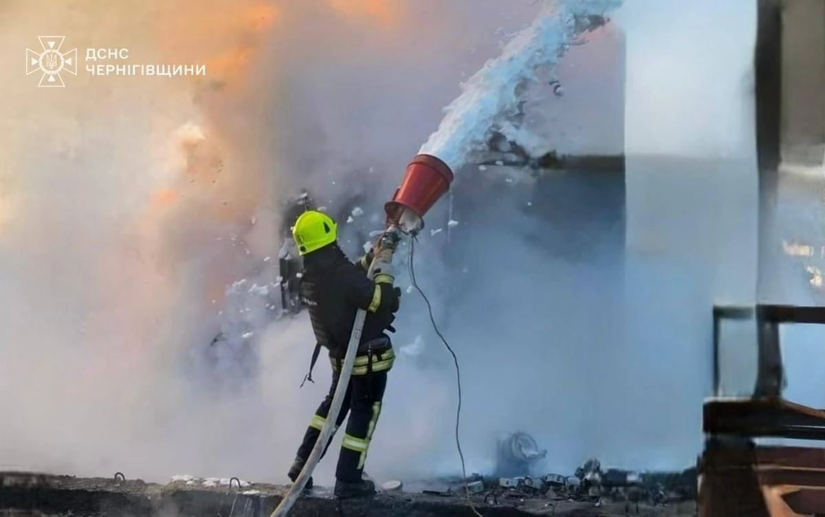 A firefighter in a bright helmet battles a fire, blasting water into heavy smoke and flames amid debris at the scene