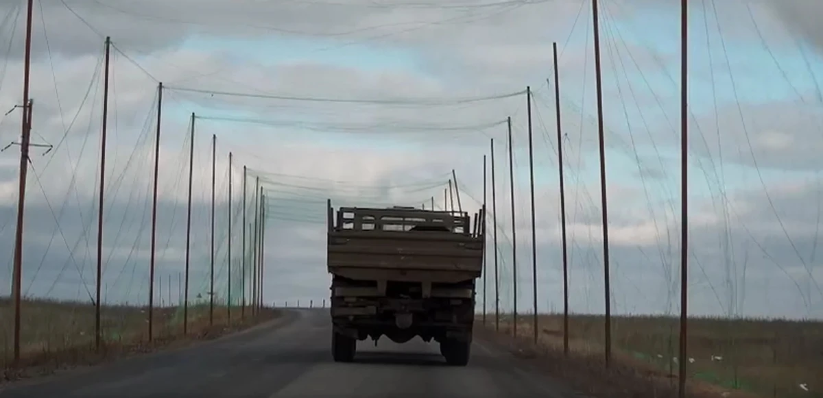 A vehicle drives along a road protected by anti-drone netting