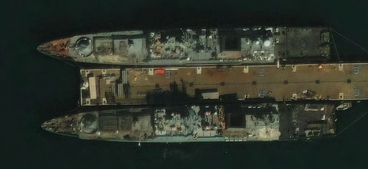 The two ships are moored on either side of the same quay, parallel to one another and facing left. Dark patches can be seen on the forward part of each deck, above the 3S14 universal launcher