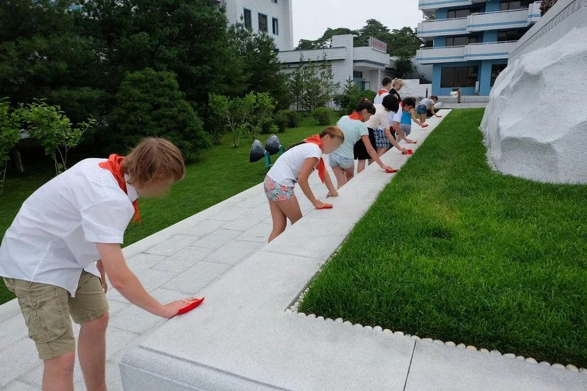 Children work at the camp – wiping down monuments to Kim Il Sung and Kim Jong Il.
