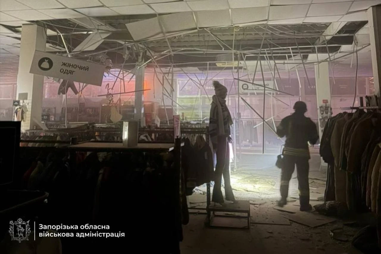 A responder with a torch inspects a clothing store after a Russian strike.