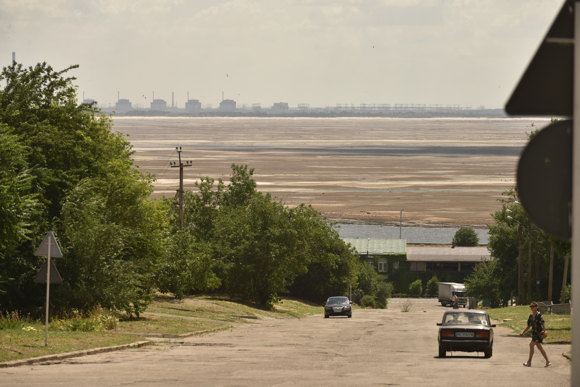 Майже сюрреалістична картина: вулиця Нікополя, буденне життя, подвір’я потопають у зелені, на заднім плані загрозливі енергоблоки Запорізької АЕС, між ними мертве Каховське море
